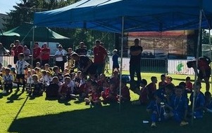 Uczestnicy turnieju siedzący na murawie boiska i oglądający mecz